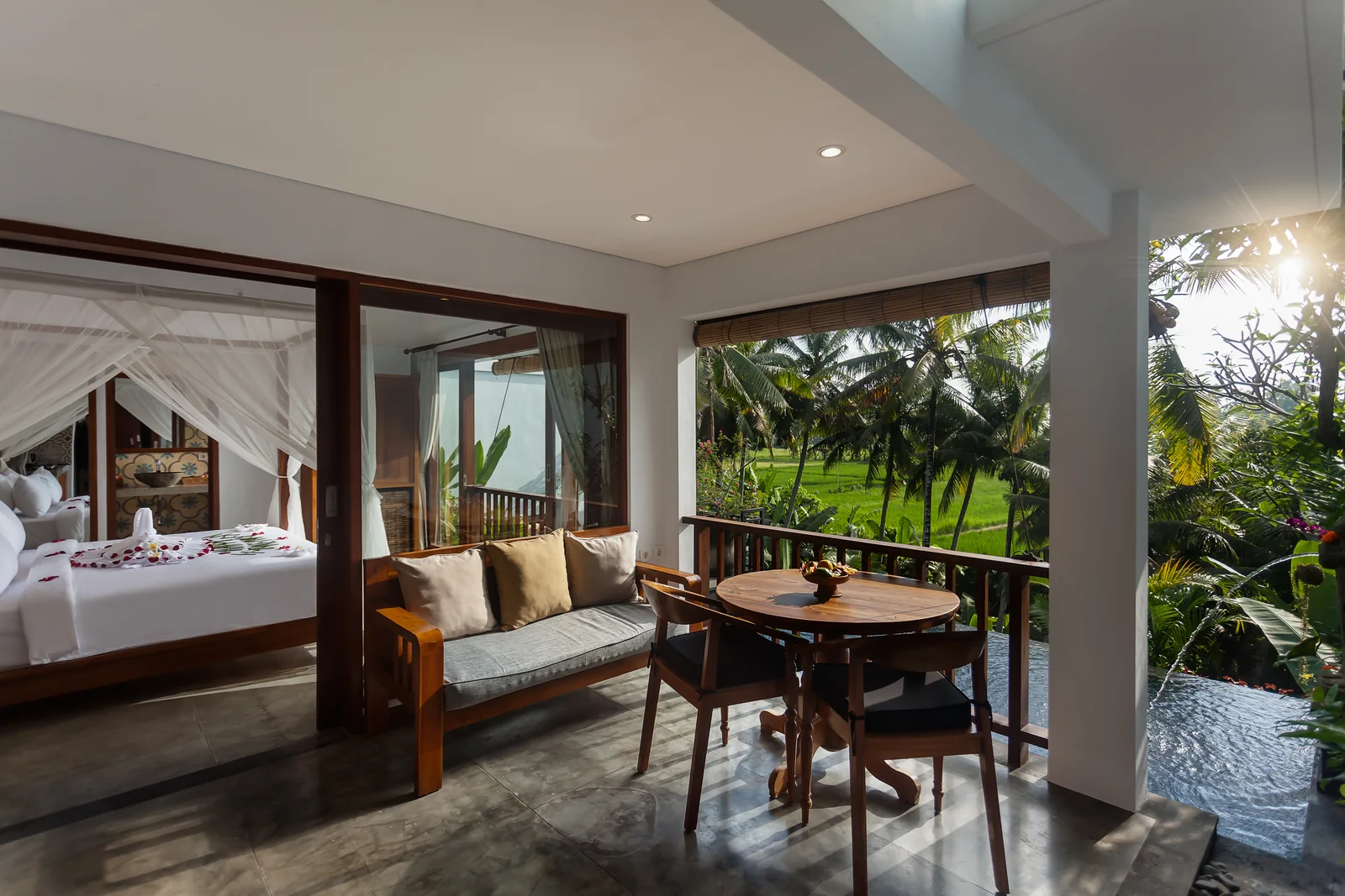 Canopy bedroom beside a covered terrace with a sofa and dining table overlooking rice fields at the 1-Bedroom Garden Villa, The Shea Ubud
