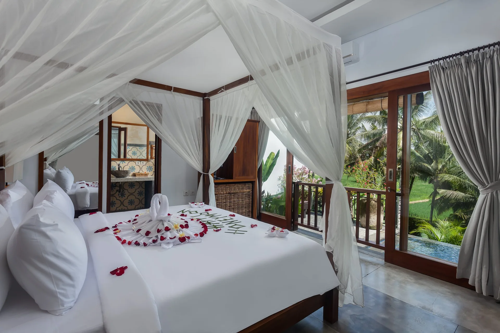 Four-poster canopy bed with white netting and rose petals beside glass doors overlooking rice fields, 2-Bedroom Tranquility Villa at The Shea Ubud
