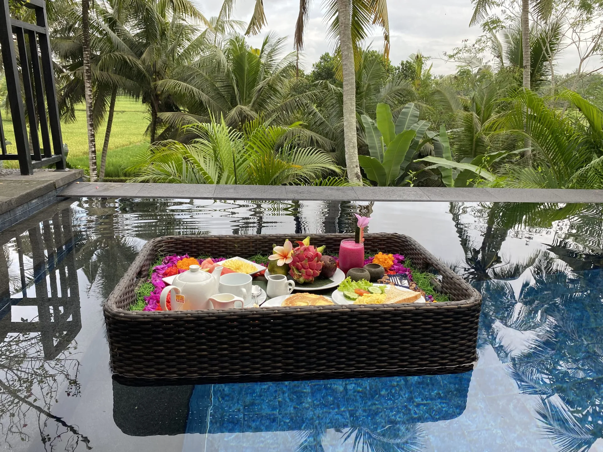 Woven floating breakfast tray with fruit, cups and plated dishes in a pool with palms and rice fields behind, 2-Bedroom Tranquility Villa at The Shea Ubud
